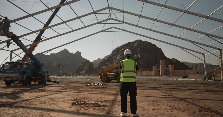 Engineer in safety vest standing at desert construction site, wide shot.