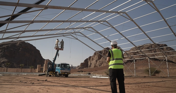 Engineer in safety vest standing at construction site in desert, wide shot.