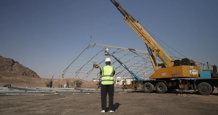 Engineer in safety vest at construction site with crane, ground shot.