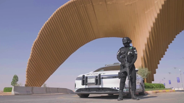 جندي يقف أمام سيارة شرطة تحت جسر منحني، لقطة نهارية.