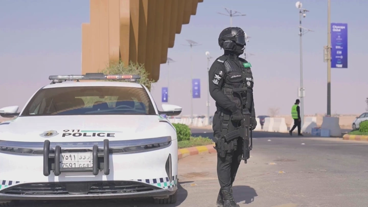 شرطي بجانب سيارة شرطة في شارع مشمس، لقطة نهارية.