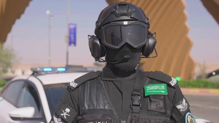 جندي يرتدي زيًا عسكريًا أمام سيارة شرطة، لقطة نهارية.