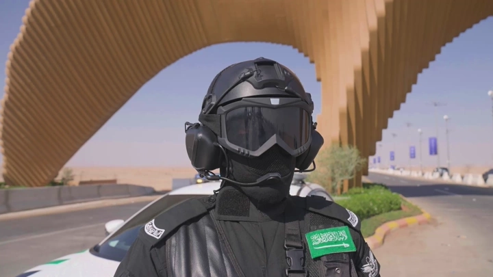 جندي يرتدي زيًا عسكريًا أسود تحت جسر في الصحراء، لقطة نهارية.