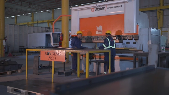 عمال في مصنع يستخدمون آلة ثني المعادن، لقطة داخلية.