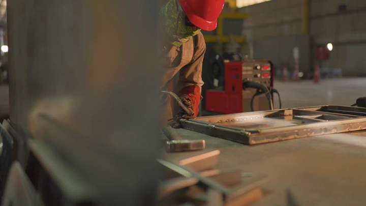 عامل يرتدي خوذة حمراء يعمل في مصنع، لقطة داخلية.