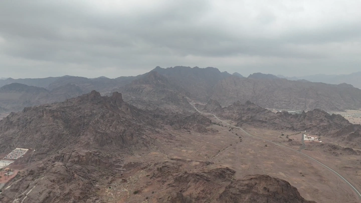 جبال صخرية تحت سماء غائمة في حائل، لقطة جوية.