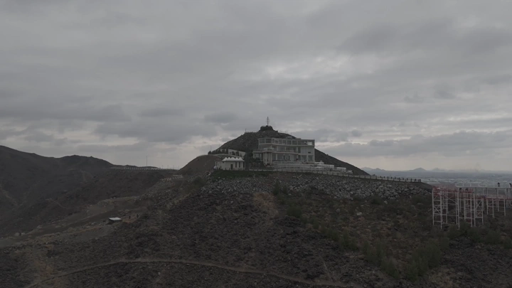 Building on a mountain peak under cloudy skies, aerial shot.