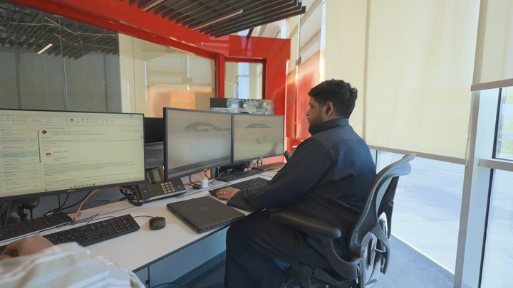 موظف يجلس في مكتب حديث مع شاشات متعددة، لقطة داخلية.