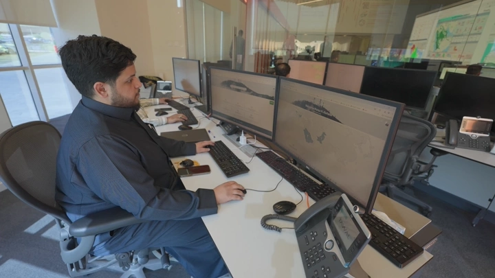 موظف يعمل على الحاسوب في مكتب حديث، لقطة داخلية.