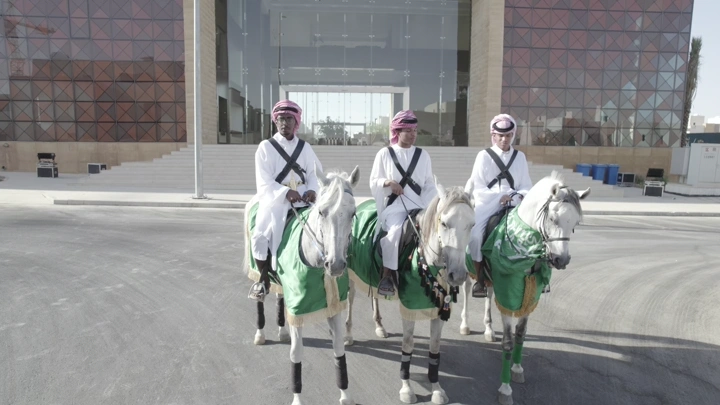 فرسان يرتدون الزي التقليدي أمام مبنى حديث، لقطة نهارية.