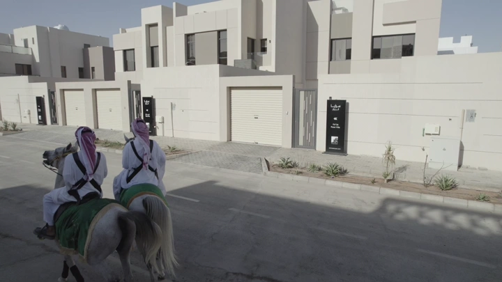 فرسان على خيول أمام منازل حديثة في حي سكني، لقطة نهارية.