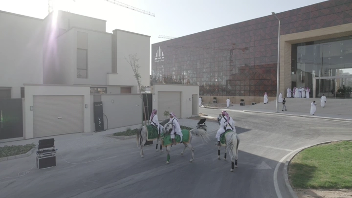 فرسان على خيول بيضاء في احتفال أمام مبنى حديث، لقطة نهارية.