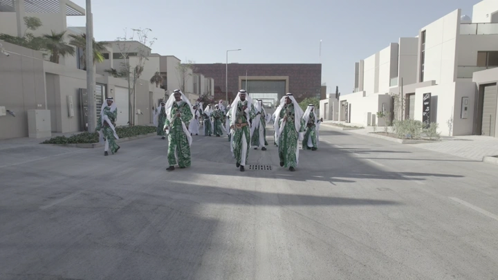 مجموعة رجال في زي تقليدي يسيرون في شارع حديث، لقطة نهارية.