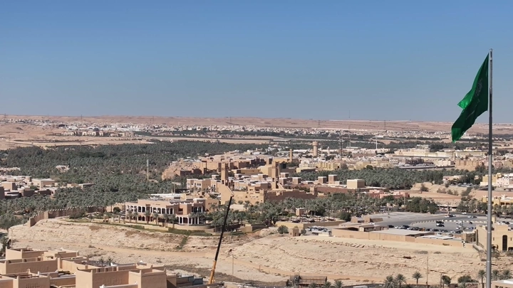 منظر علوي لمدينة الدرعية مع سارية علم السعودية، في يوم مشمس.