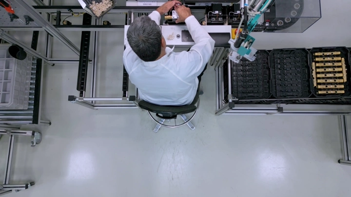 عامل في مصنع يجلس على كرسي ويعمل على خط إنتاج، لقطة علوية.