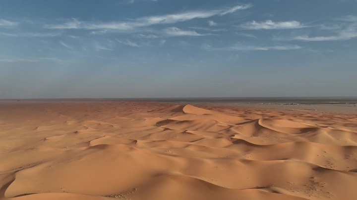 كثبان رملية في الصحراء تحت سماء زرقاء، لقطة جوية.