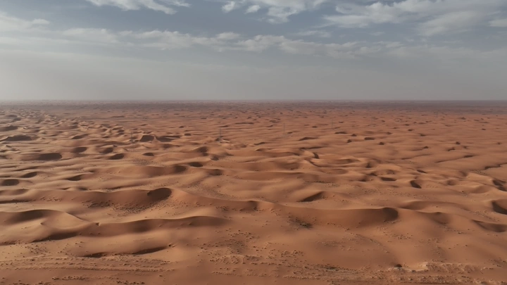 كثبان رملية في الصحراء تحت سماء غائمة، لقطة جوية.