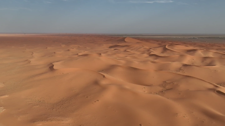 كثبان رملية في صحراء النفود تحت سماء زرقاء، لقطة جوية.