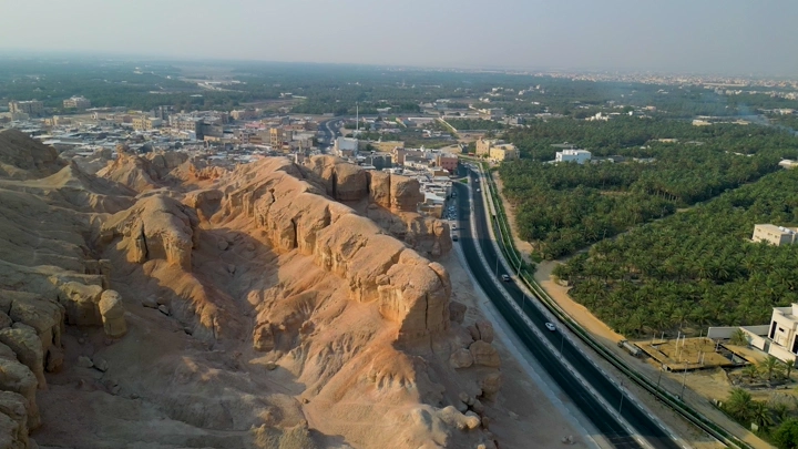 جبل القارة في الأحساء مع طريق ومزارع نخيل، لقطة جوية.