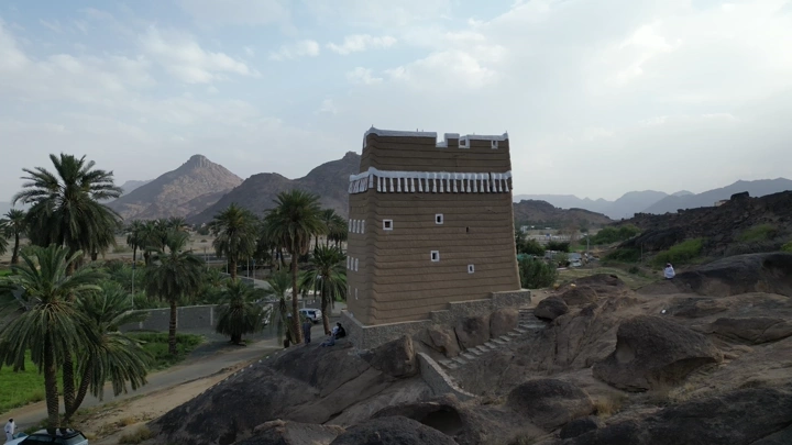 Traditional mud house in Najran surrounded by palm trees and mountains, aerial shot.