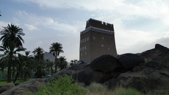 بيت طيني تقليدي في نجران محاط بالنخيل، لقطة نهارية.