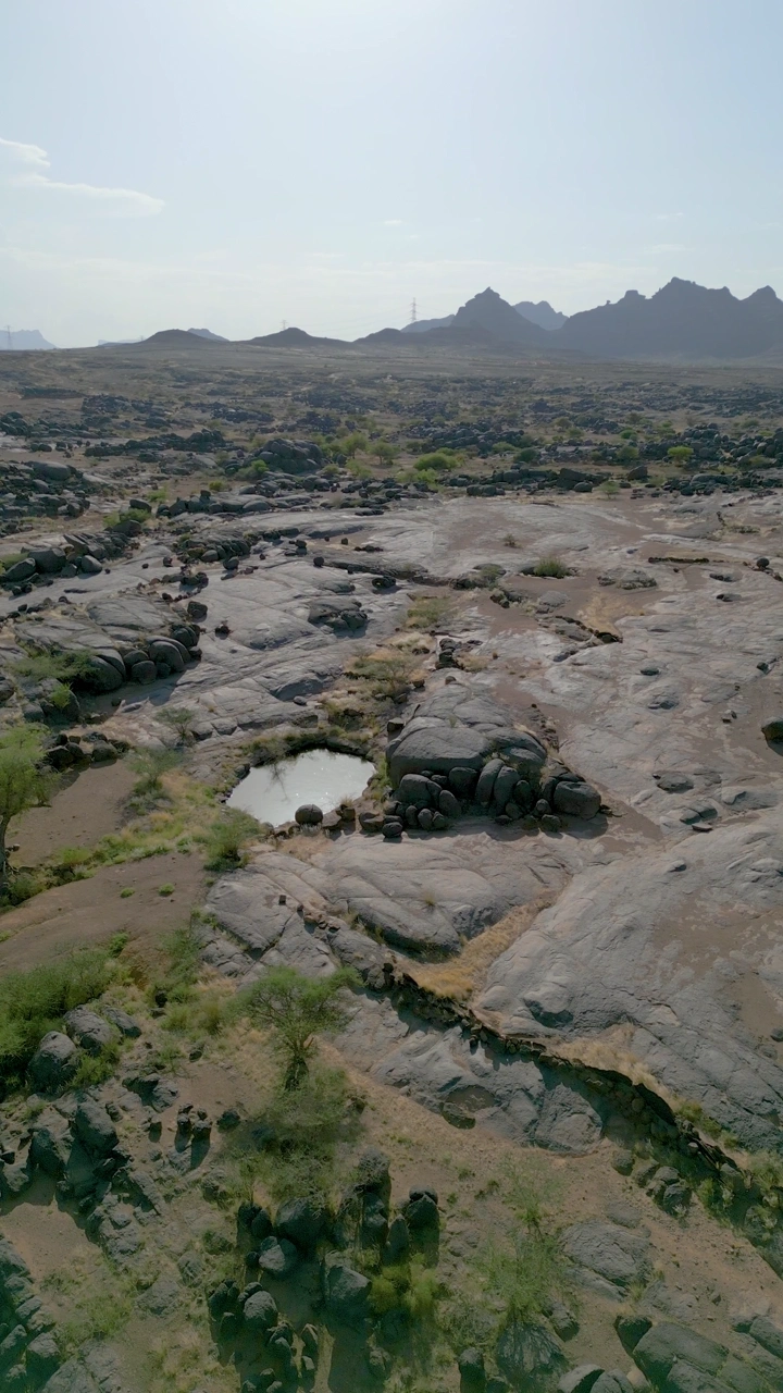 منظر جوي لبئر عسكر في نجران، مع تضاريس صخرية وجبال في الأفق.