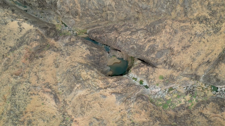 لقطة جوية لجبل مغرة في نجران، تُظهر تضاريس صخرية مع بركة مياه صغيرة.