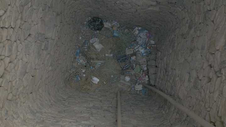 بئر حجري قديم يحتوي على نفايات في قرية المشكاة نجران، لقطة من الأعلى.