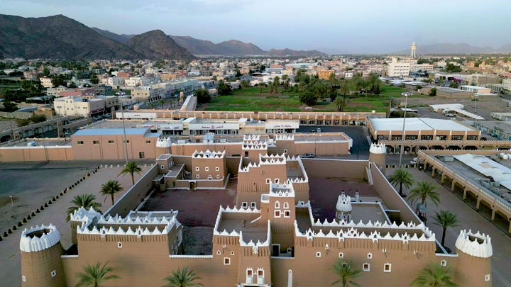 قصر تاريخي في نجران محاط بالمباني والجبال، لقطة جوية.