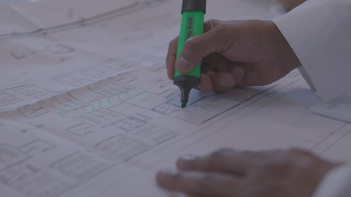 يد تضع علامة على مخطط معماري باستخدام قلم تحديد أخضر، لقطة مقربة.