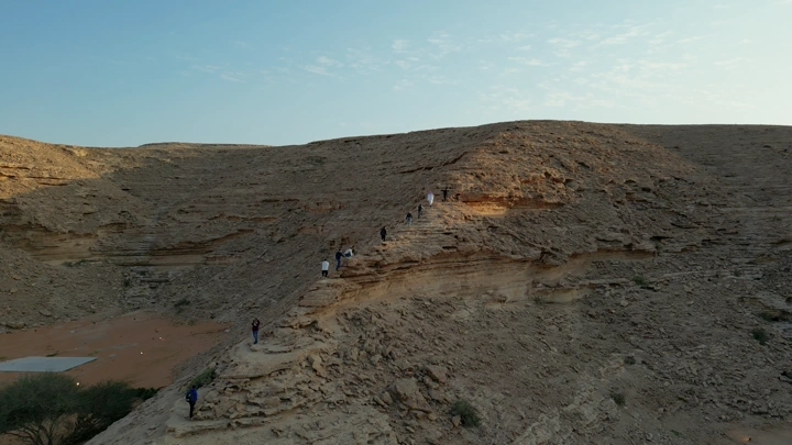 مجموعة تتسلق جبلًا في الصحراء عند الغروب، لقطة جوية.
