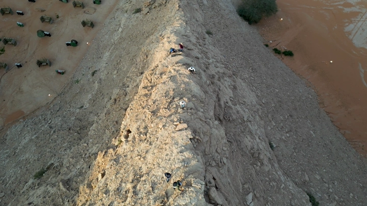 أشخاص يتسلقون جبلًا صخريًا في الصحراء، لقطة جوية.