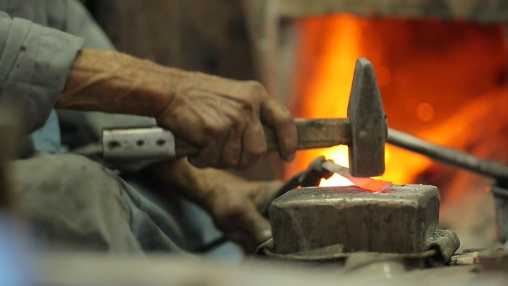 حداد يعمل على الحديد في ورشة، لقطة قريبة.