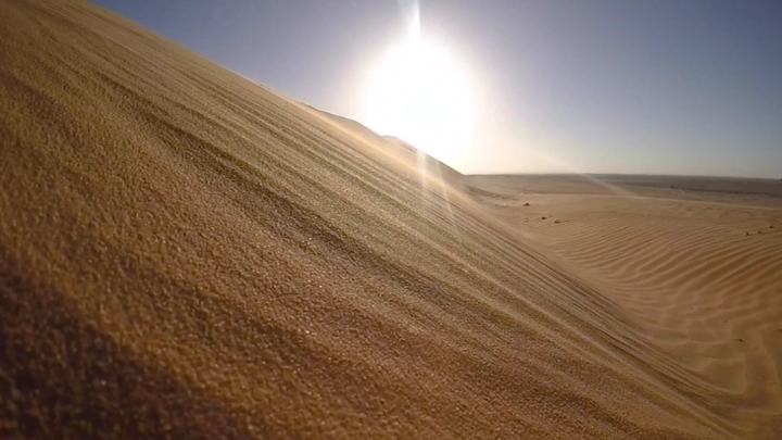 كثبان رملية في الصحراء تحت شمس مشرقة، لقطة واسعة.