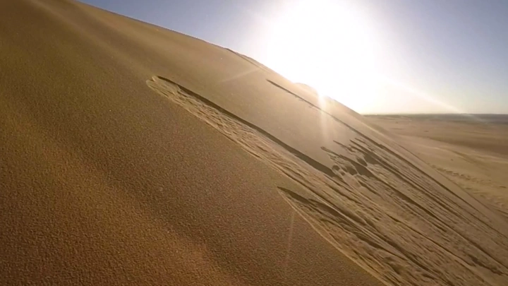 كثبان رملية في الصحراء تحت أشعة الشمس، لقطة بزاوية مائلة.