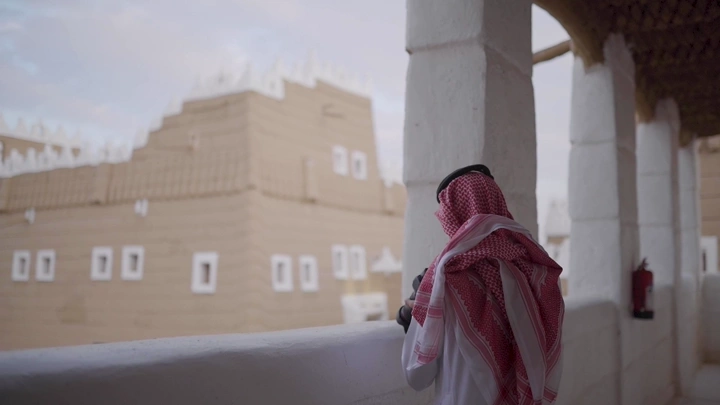 رجل يرتدي الزي التقليدي ينظر إلى قصر تاريخي في نجران، لقطة جانبية.