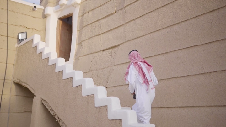 رجل يرتدي الزي التقليدي يصعد درج قصر الإمارة في نجران، لقطة جانبية.