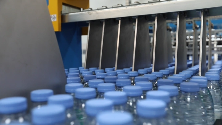 زجاجات مياه على خط إنتاج في مصنع، لقطة قريبة.