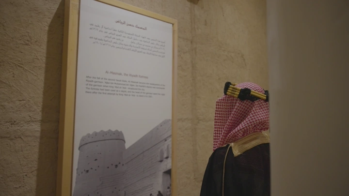 شخص يرتدي الزي التقليدي ينظر إلى لوحة في قصر المصمك، لقطة داخلية.