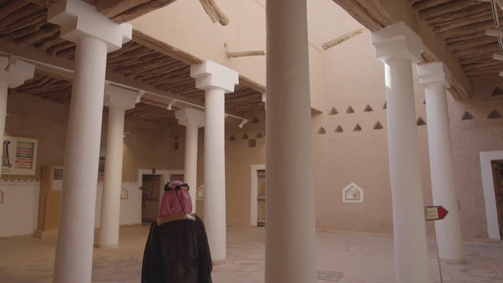 داخل قصر المصمك شخص يمشي ويرتدي الزي السعودي ليوم التاسيس في الرياض، لقطة داخلية.