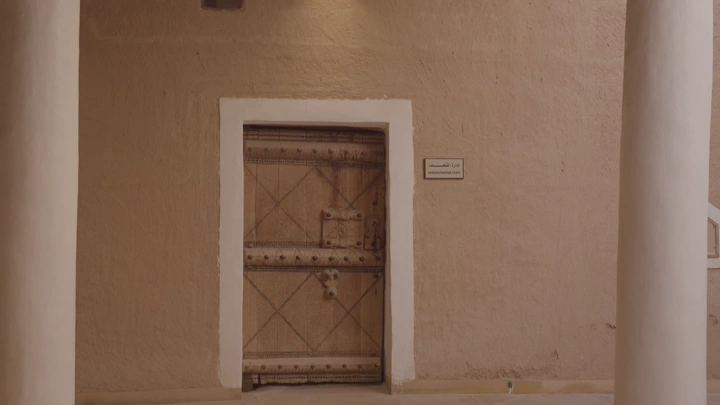 باب خشبي مع شخص يمشي ويرتدي الزي السعودي ليوم التاسيس في قصر المصمك بالرياض، لقطة قريبة.