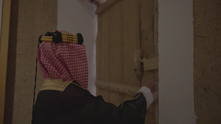 رجل يرتدي الزي التقليدي يفتح باب قصر المصمك في الرياض، لقطة داخلية.