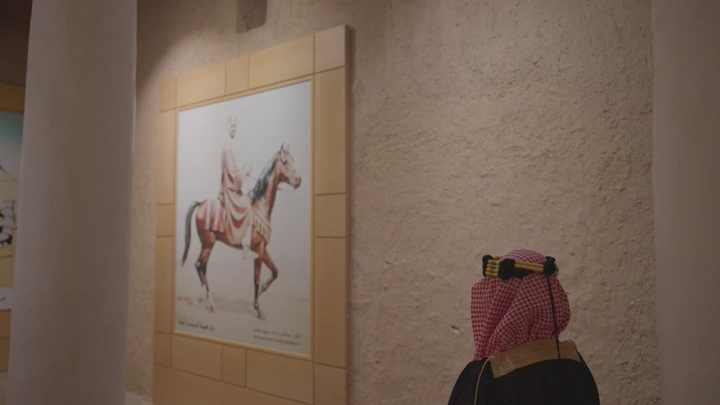 رجل يرتدي الزي التقليدي ينظر إلى لوحة في قصر المصمك، لقطة داخلية.