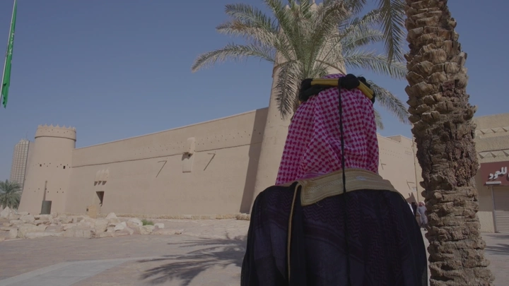 رجل يرتدي الزي التقليدي ليوم التاسيس أمام قصر المصمك في الرياض، لقطة نهارية.