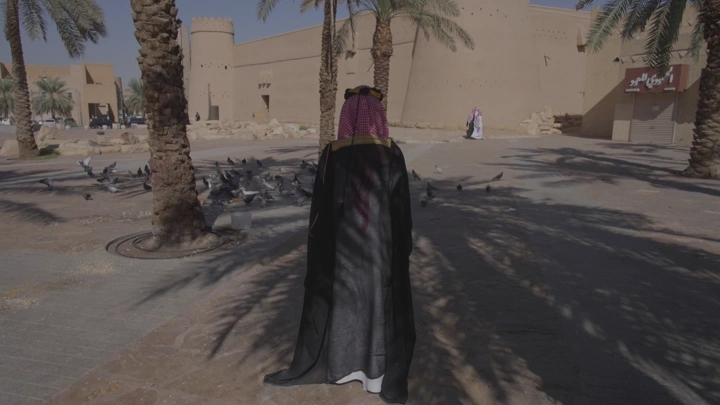 رجل يرتدي الزي التقليدي ليوم التاسيس أمام قصر المصمك في الرياض، لقطة نهارية.