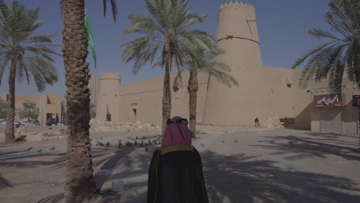 قصر المصمك في الرياض نهارًا، لقطة من الخلف لشخص يرتدي الزي التقليدي.