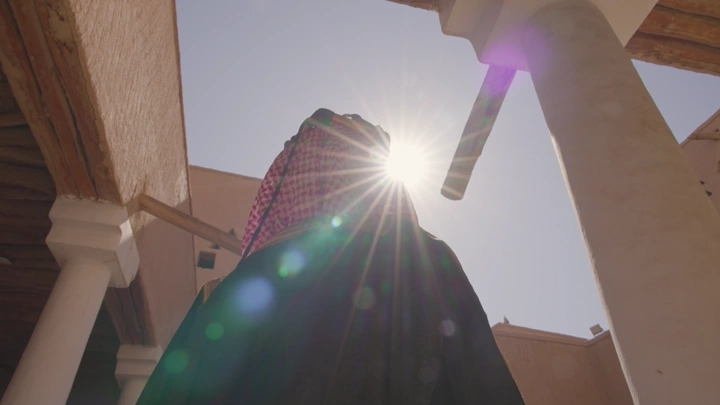 شخص يرتدي الزي التقليدي ليوم التاسيس في قصر المصمك بالرياض، لقطة من الأسفل مع الشمس.