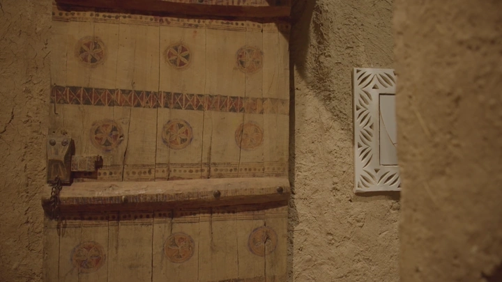 باب خشبي مزخرف ورجل يمشي بزي التقليدي ليوم التاسيس في قصر المصمك بالرياض، لقطة قريبة.