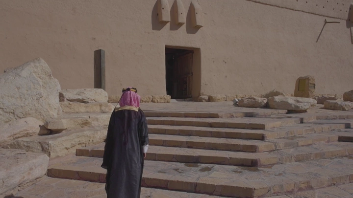 رجل يرتدي الزي التقليدي ليوم التاسيس أمام قصر المصمك في الرياض، لقطة نهارية.