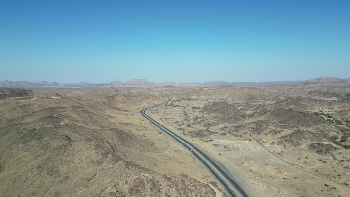 طريق سريع يمتد عبر الصحراء تحت سماء زرقاء، لقطة جوية.